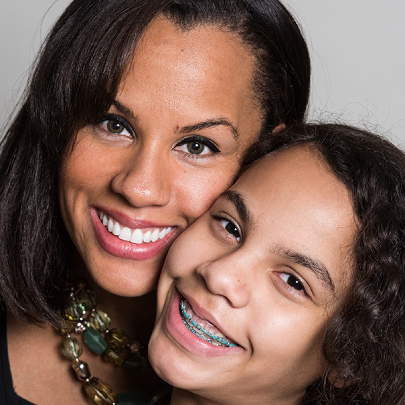 Picture of a mother and daughter smiling together, the daughter is wearing braces