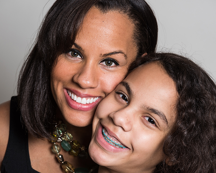 Picture of a mother and daughter smiling together, the daughter is wearing braces